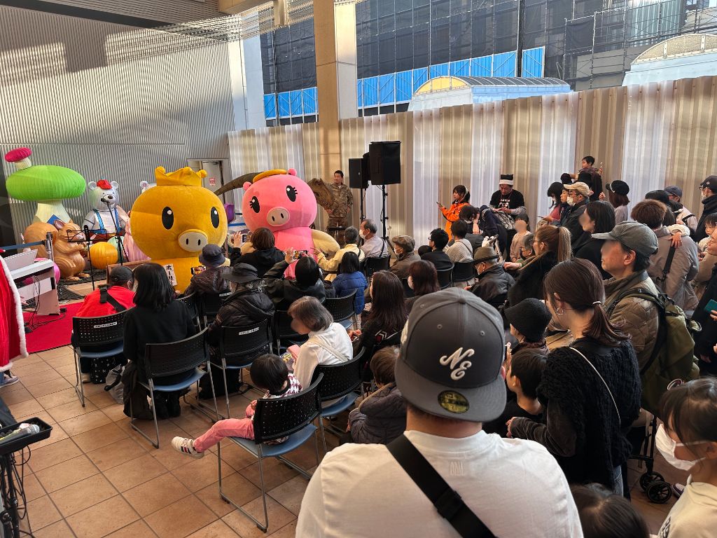 イルミネーション点灯式のステージに恐竜が参加。キャラクターと共演し、大勢の観覧者が座席から見守る様子